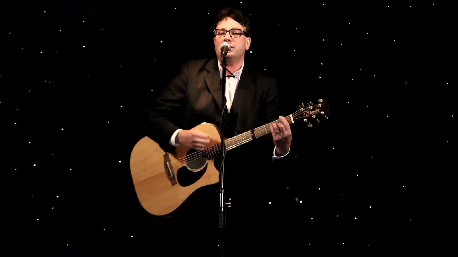 Tony Costello mid-song on a dark stage